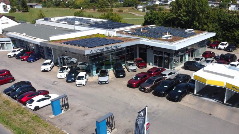 Das Autohaus mit mehreren Fahrzeugen und modernen Gebäuden, umgeben von Grünflächen. Bildwinkel entspricht einer Drohnenaufnahme.