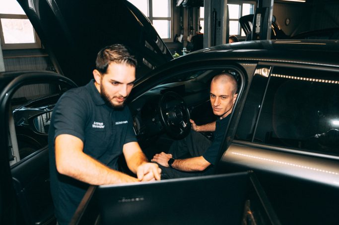 Zwei Techniker arbeiten an einem Fahrzeug und analysieren Daten an einer Diagnosestation.