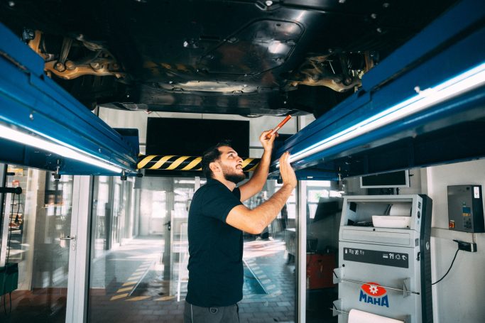 Ein Mechatroniker arbeitet unter einem Auto auf der Hebebühne in der Werkstatt und überprüft das Auto.